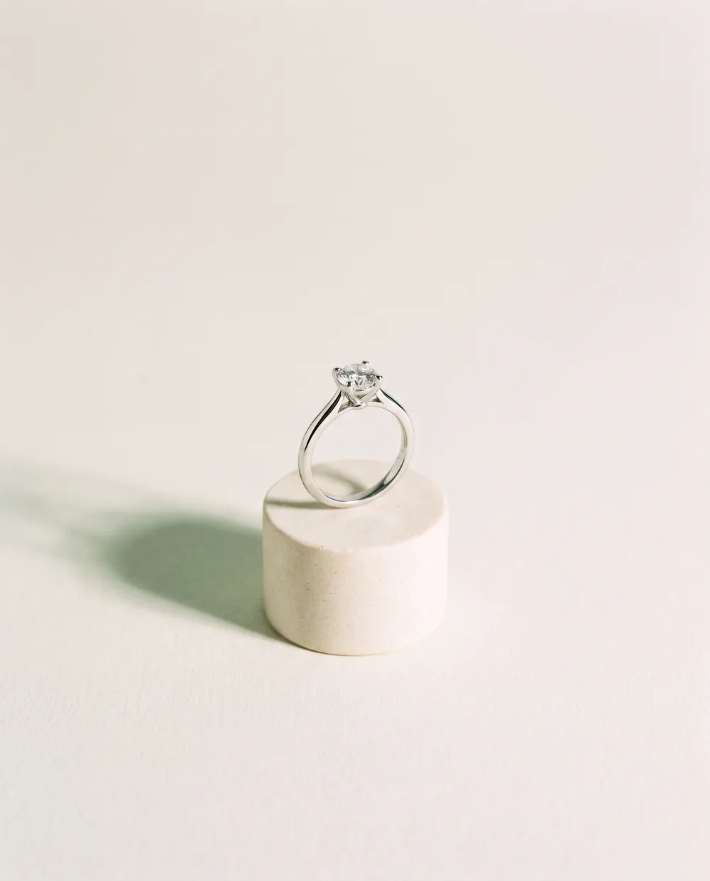 A finished platinum solitaire engagement ring on a cream pedestal