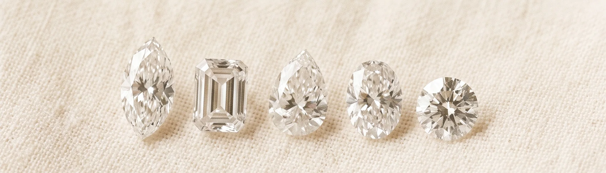 Loose diamonds in five shapes — marquise, emerald, pear, oval and round — on cream linen