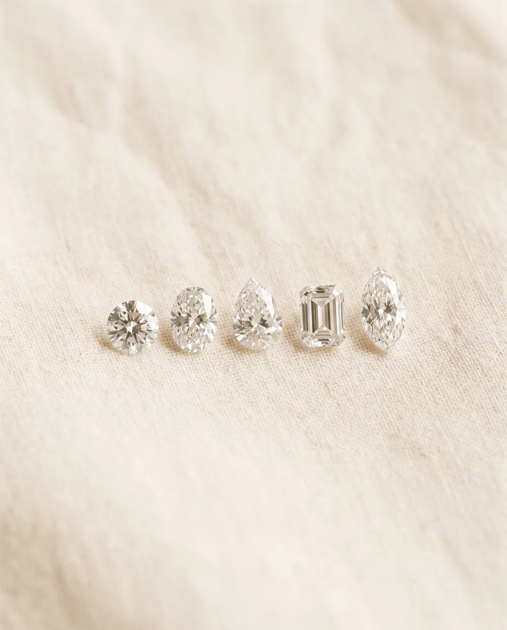 Five loose diamonds in different shapes on cream linen